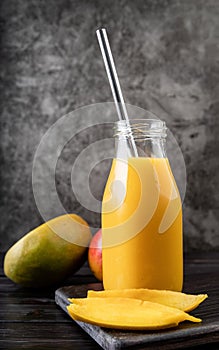 Fresh mango shake in a glass with a metal drinking straw decorated with slices of mango front view on dark background