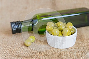 Fresh marinated green olives in white ceramic bowl and green bottle of premium virgin olive oil  on  burlap cloth background