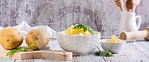 Fresh mashed potatoes and basil leaves in a bowl and whole potatoes on the table web banner