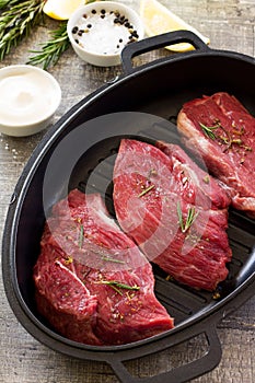 Fresh meat. Raw steak beef on a cast-iron grill frying pan, olive oil, spices and fresh rosemary on the kitchen table