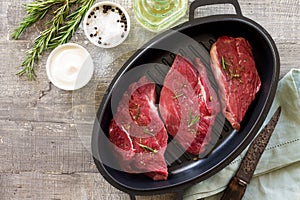 Fresh meat. Raw steak beef on a cast-iron grill frying pan, olive oil, spices and fresh rosemary on the kitchen table. Flat lay.