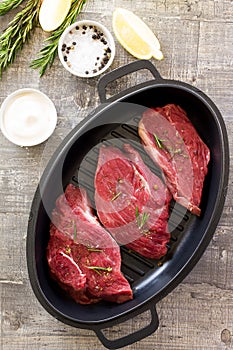 Fresh meat. Raw steak beef on a cast-iron grill frying pan, olive oil, spices and fresh rosemary on the kitchen table. Flat lay.