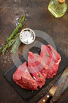 Fresh meat. Raw steak beef on a slate cutting board, olive oil, spices and fresh rosemary on a stone background.