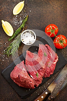 Fresh meat. Raw steak beef on a slate cutting board, tomatoes, olive oil, spices and fresh rosemary on a stone table.