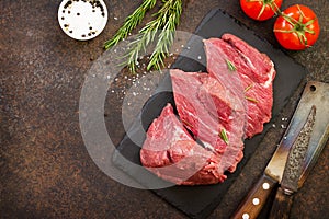 Fresh meat. Raw steak beef on a slate cutting board, tomatoes, olive oil, spices and fresh rosemary on a stone table. Flat lay.