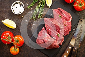 Fresh meat. Raw steak beef on a slate cutting board, tomatoes, olive oil, spices and fresh rosemary on a stone table. Flat lay.