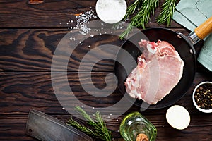 Fresh meat. Raw steak cutlet on a bone on a cast-iron frying pan, olive oil, spices and fresh rosemary on the kitchen table.