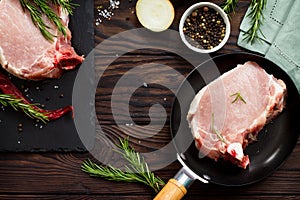 Fresh meat. Raw steak cutlet on a bone on a cast-iron frying pan, olive oil, spices and fresh rosemary on the kitchen table.