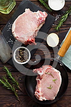 Fresh meat. Raw steak cutlet on a bone on a cast-iron frying pan, olive oil, spices and fresh rosemary on the kitchen table. Flat