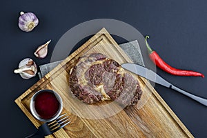 Fresh meat steak and seasonings on rustic wooden board over black background. Top view, flat lay, copy space banner.