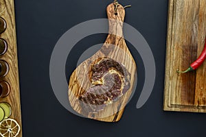 Fresh meat steak and seasonings on rustic wooden board over black background. Top view, flat lay, copy space banner.