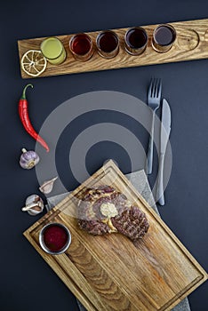 Fresh meat steak and seasonings on rustic wooden board over black background. Top view, flat lay, copy space banner.