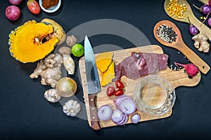 Fresh meats on a cutting board with vegetables and spices.