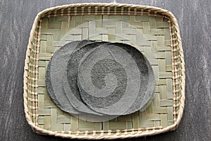 Fresh Mexican made blue corn tortillas ready to eat in taco on wooden table with woven base woven basket