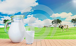 Fresh milk in clear glass and milk jug on the reflective plank floor. Bright green grassland cows are walking freely and enjoying