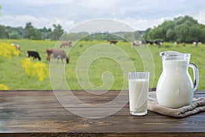 Fresh milk in glass on dark wooden table and blurred landscape with cow on meadow. Healthy eating. Rustic style.