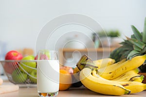 Fresh milk in a glass is placed on a wooden table among fruits