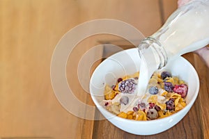 fresh milk on the white cup, cornflakes cereal, strawberry, blackberry and milk in a white bowl, selective focus.