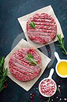 Fresh minced beef meat burgers with spices on dark background. Raw ground beef meat