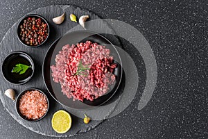 Fresh minced meat ground beef on a black plate against stone background.