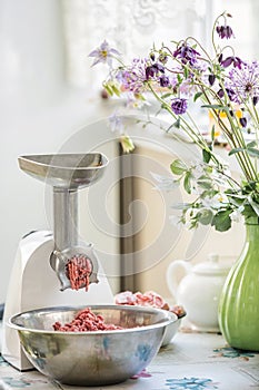 Fresh minced meat twisted in a meat grinder. In a beautiful kitchen with flowers. Forcemeat in a bowl