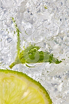 Fresh mint leaf and a slice of lime with bubbles in a glass with ice. Macro photo of refreshing drink
