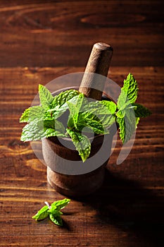 Fresh mint leafs in vintage mortar on wooden table