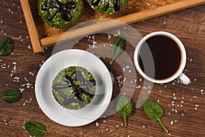 Fresh muffins with spinach, desiccated coconut, chocolate glaze and cup of coffee, delicious healthy dessert