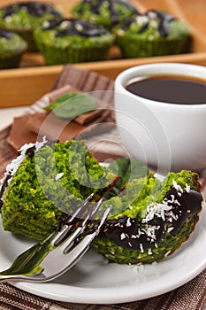 Fresh muffins with spinach, desiccated coconut, chocolate glaze and cup of coffee, delicious healthy dessert