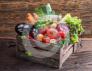 Fresh multi-colored vegetables in wooden crate. Wooden background.