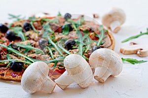 Fresh mushrooms on the white table with free copy space on the right side. Veggie pizza with vegetables, olives, rucola