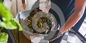 Fresh mussels in copper dish in hands. Waiter with a big bowl of mussels in a restaurant.