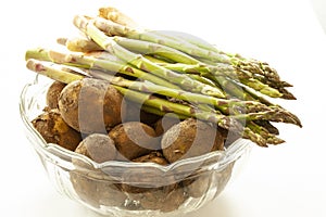 Fresh new potatoes with peel on and green asparagus in a glass bowl. Close up image on white background