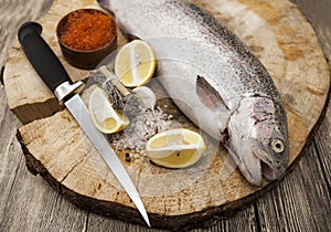 Fresh Norwegian rainbow trout with lemon red caviar, sea salt, knife and onions on a wooden background