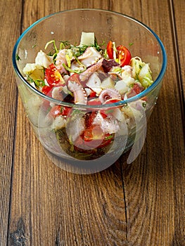 Fresh octopus salad in a glass bowl on a wooden table, Portrait orientation, healthy food