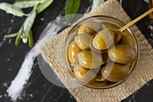 Fresh olives in a glass bowl with a golden spoon on a dark textured background