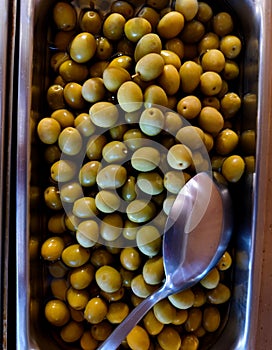 Fresh olives in a refrigerated container with a spoon in a restaurant