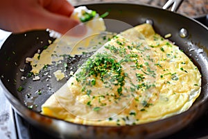 fresh omelet on skillet, someone garnishing it with herbs