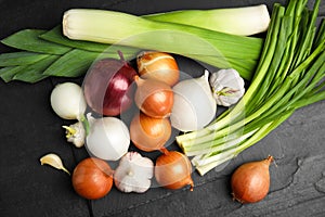 Fresh onion bulbs, leeks and garlic on black table, flat lay