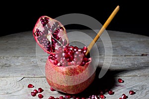 Fresh Open Pomegranate with Wooden Spoon on an Rustic Wooden Table, Black Background