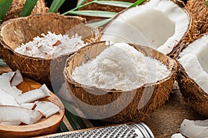 Fresh opened coconuts along with coconut slices, flakes and coconut leaves on a wooden table.