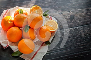 Fresh orange fruits with leaves on napery on wooden table and sunlight morning