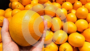 An orange on a hand with group of oranges in supermarket