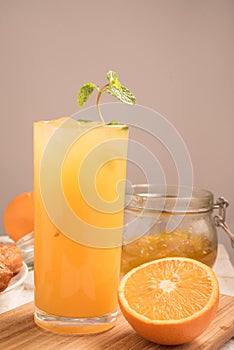Fresh orange juice in a glass on a wooden panel with jam and half orange.