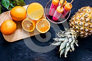Fresh orange juice, oranges, pineapple and citrus ice cream on black table background top view copyspace