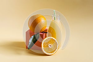 Fresh orange juice in a transparent bottle with a decor of oranges and green leaves on a yellow backgroun