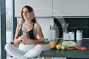 With fresh orange juice. Young european woman is indoors at kitchen indoors with healthy food