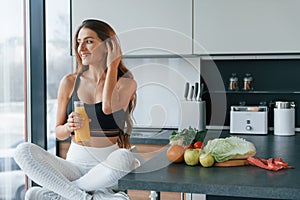 With fresh orange juice. Young european woman is indoors at kitchen indoors with healthy food