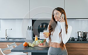 With fresh orange juice. Young european woman is indoors at kitchen indoors with healthy food