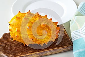 Fresh orange kiwano cucumis metuliferus, horned melon on a brown wooden cutting board. Fruits, vegetables, vegetarian and